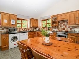 A kitchen with wooden cabinets, a microwave, a washing machine, and a dining table with chairs.