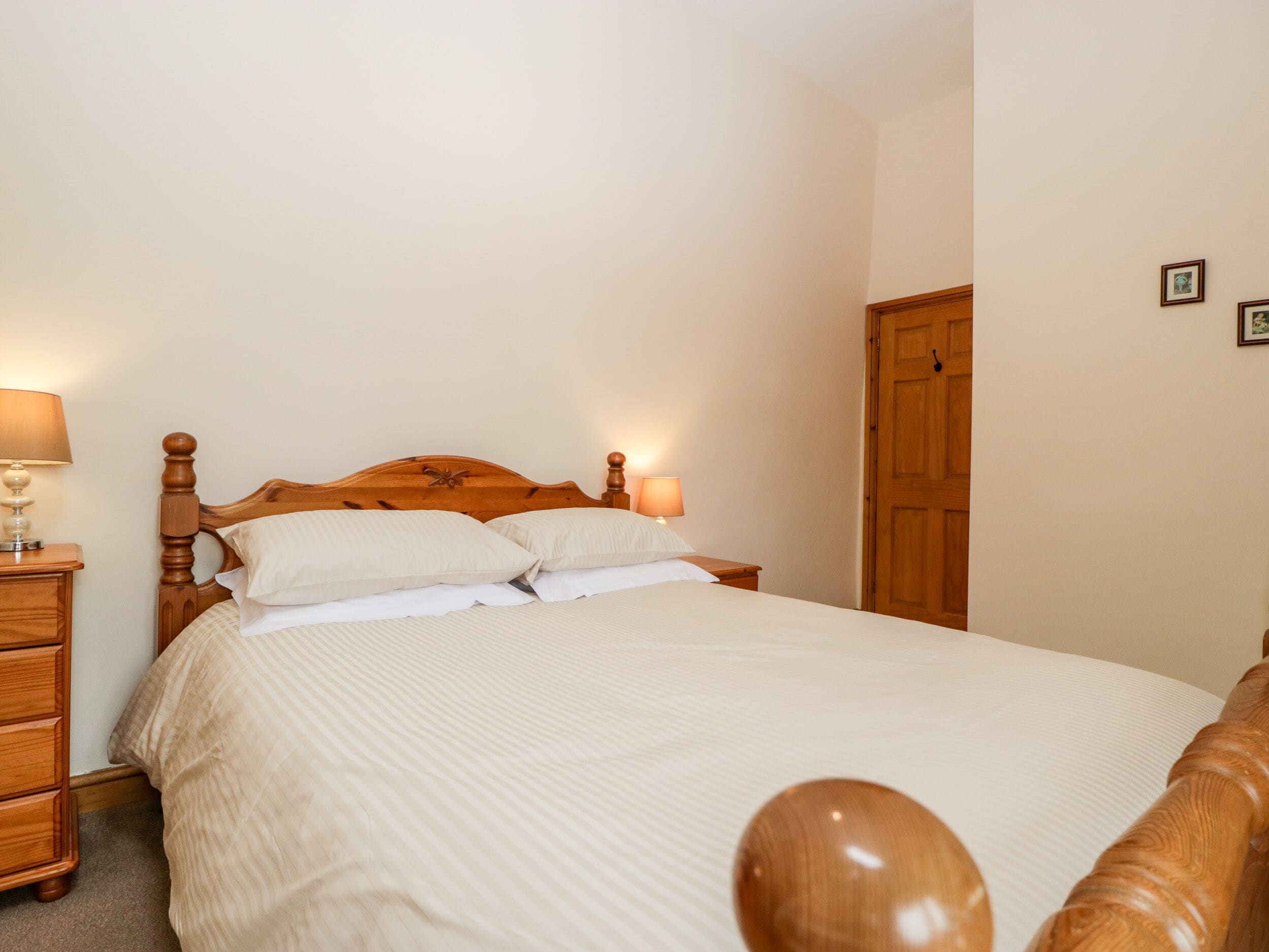 A neatly made bed with a wooden headboard, a wooden nightstand with a lamp, and a wooden wardrobe.