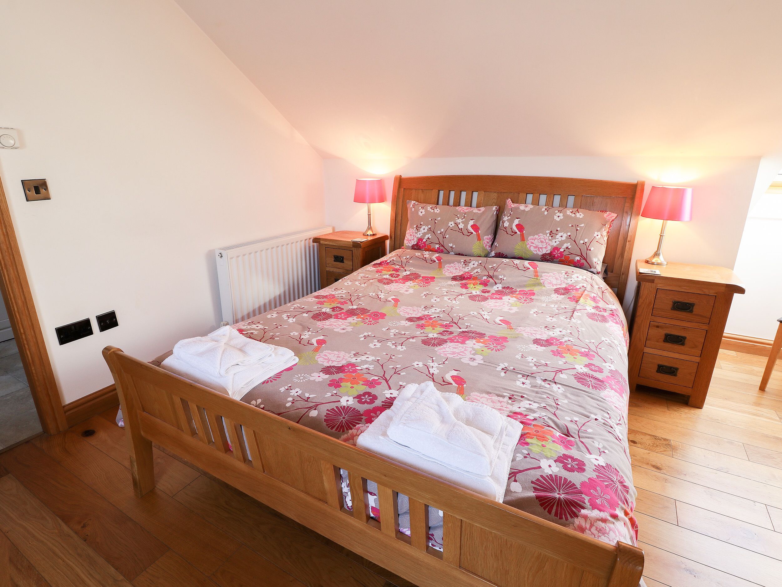 Une chambre à coucher avec un lit en bois, une literie à motifs floraux, deux lampes de chevet, une table de chevet en bois et un radiateur.