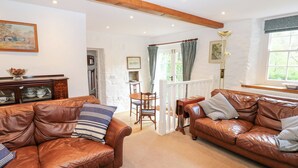 A spacious living room with leather sofas, a wooden coffee table, and a dining area with a table and chairs. - Farrier's Cottage (Sedbergh)