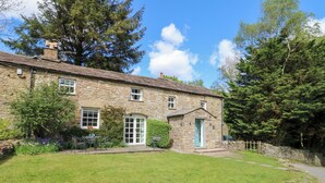A stone house with a well-maintained lawn, a small garden, and a stone wall. - Farrier's Cottage (Sedbergh)