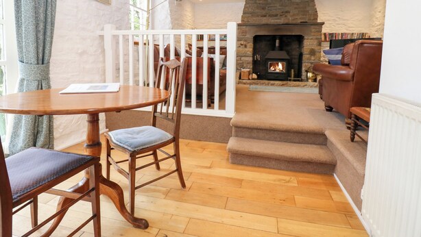 A cozy living room with a stone fireplace, wooden furniture, and a view through a white railing. - Farrier's Cottage (Sedbergh)