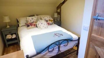 A bedroom with a bed, pillows, a nightstand, and a wooden floor.