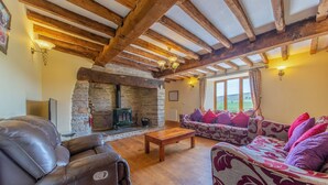 A cozy living room with a stone fireplace, leather sofa, and wooden beams. - Maesgwyn (Llandrindod Wells)