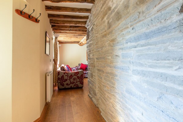 A narrow hallway with wooden floors, a stone wall on the right, and a sofa with patterned cushions in the background.