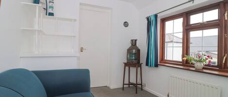 A room with a blue sofa, a small table with a lantern, a window with curtains, and a radiator.