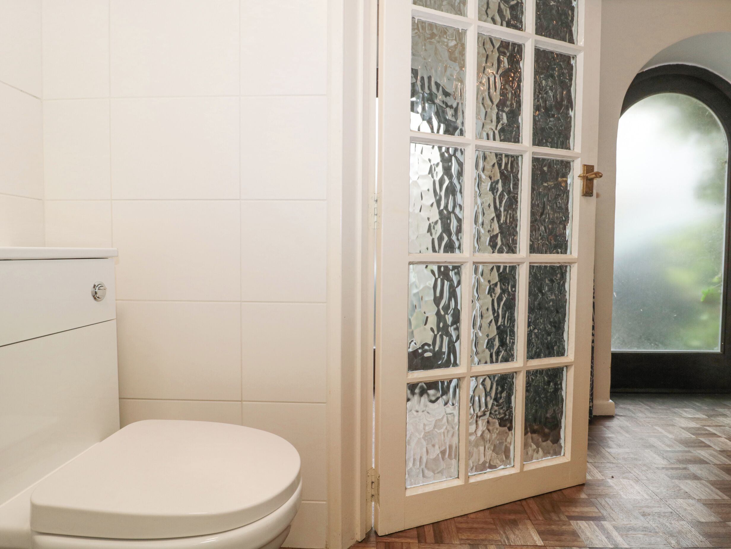 A bathroom with a white toilet, a white tiled wall, and a door with frosted glass panels.