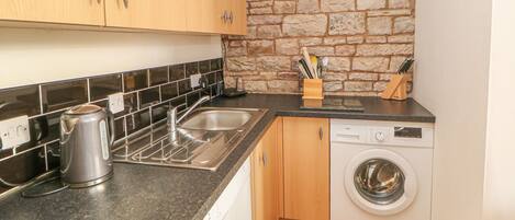 A compact kitchen with a sink, kettle, and a washing machine.