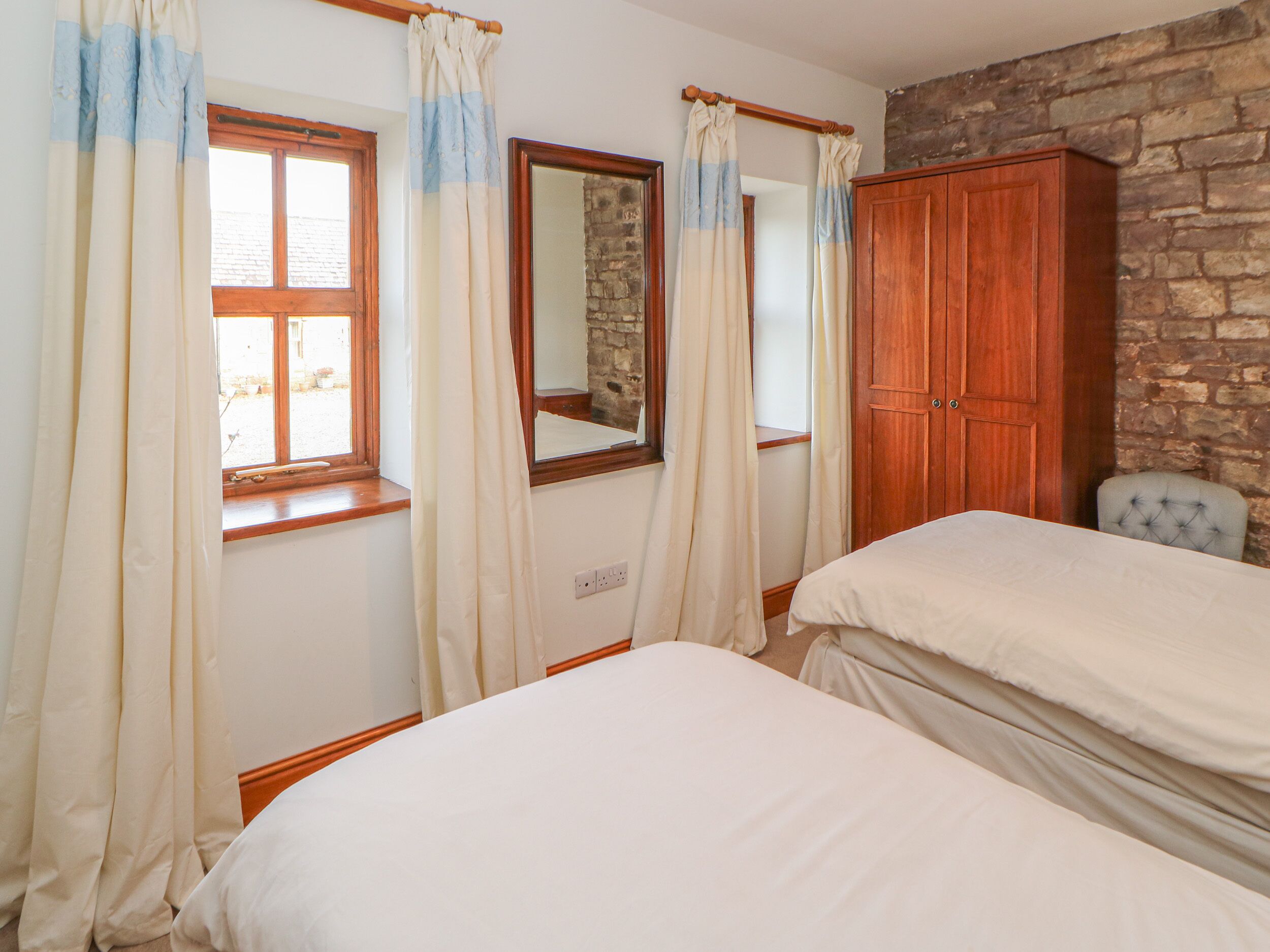 Un dormitorio con dos camas, un armario de madera, una pared de piedra y una ventana con cortinas.