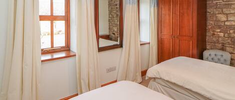 Un dormitorio con dos camas, un armario de madera, una pared de piedra y una ventana con cortinas.