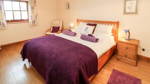 A bedroom with a wooden bed, a chair, a bedside table with a lamp, and a window with curtains. - Croft House (Ashbourne)