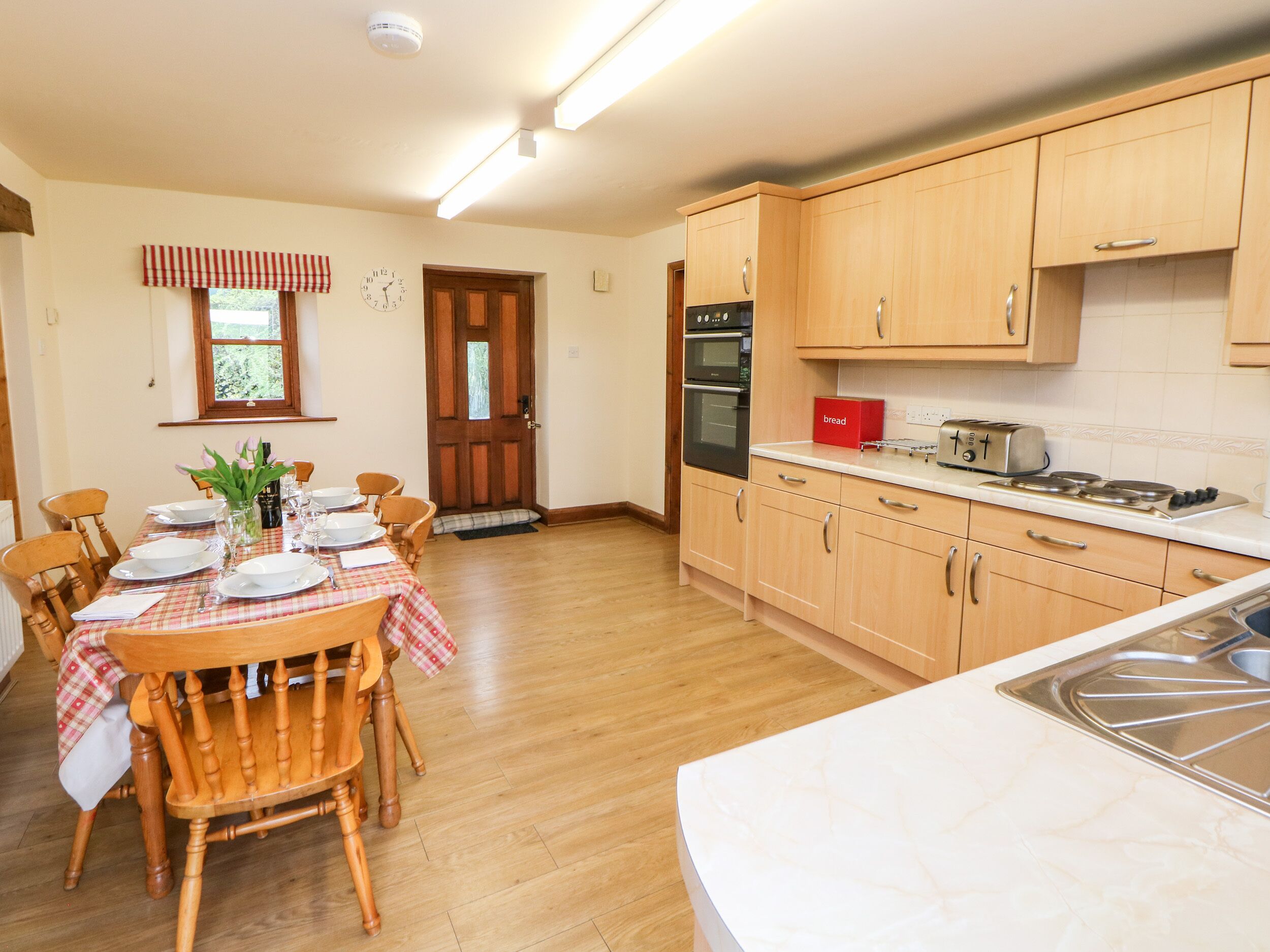 A kitchen with wooden cabinets, a dining table set with plates and glasses, and a red bread box.