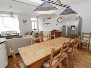 A dining area with a wooden table and chairs, a sofa, a refrigerator, and a hanging light fixture. - Rose Cottage (Cardigan)