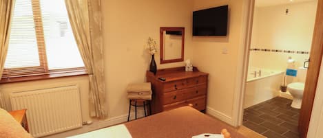 A hotel room with a bed, a vanity with a mirror, a television on the wall, and a bathroom with a bathtub and toilet.