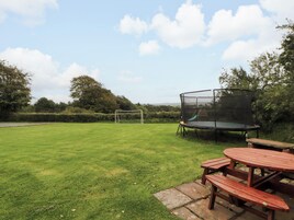 A grassy outdoor area with a trampoline, picnic tables, and a soccer goal.
