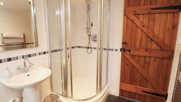 Un baño con ducha de vidrio, lavamanos y puerta de madera.