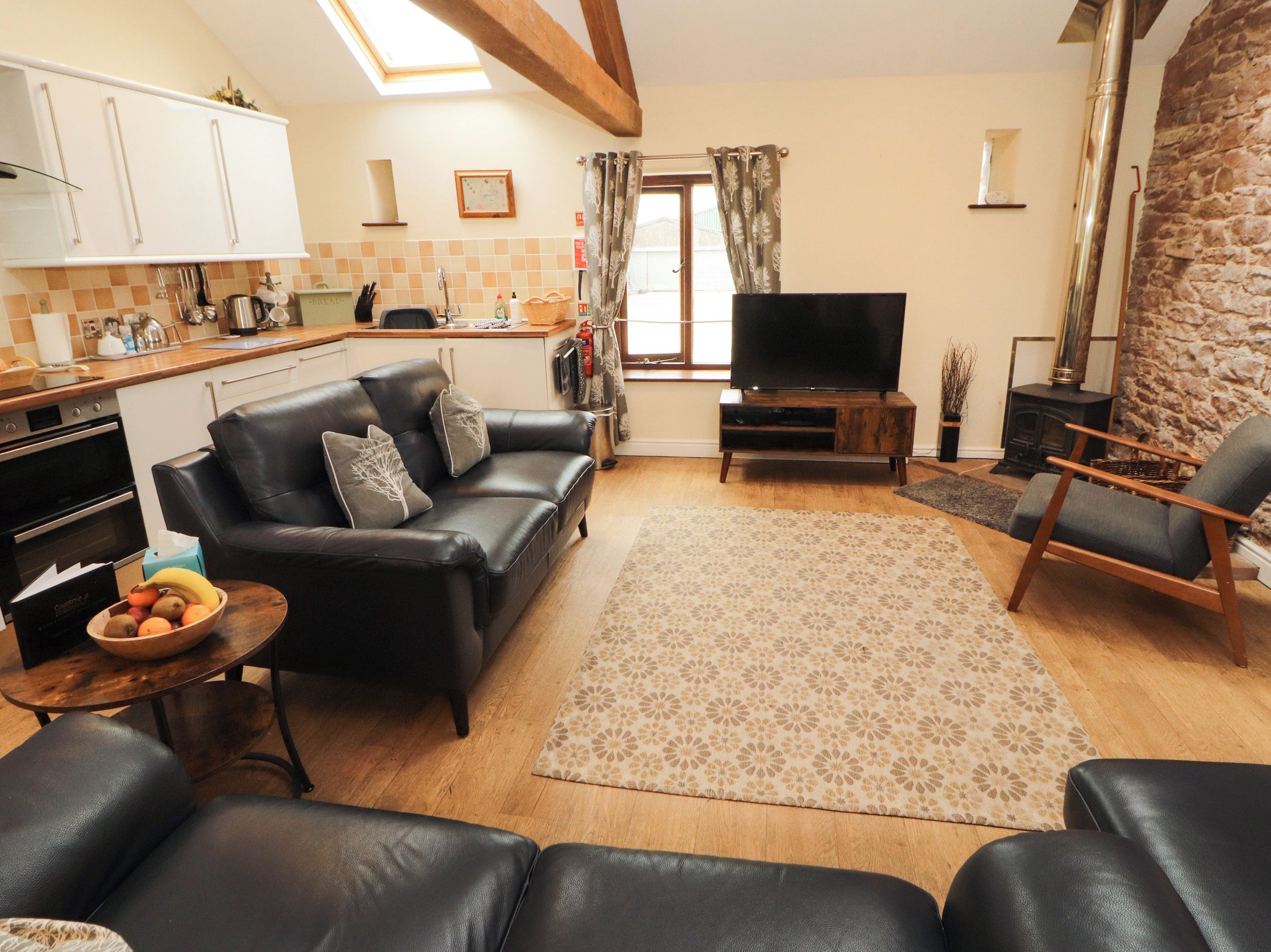 A living room with a sofa, a television, a fireplace, and a kitchen area.