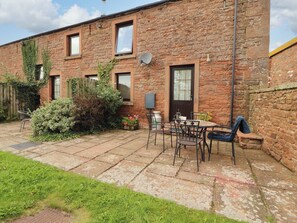 A stone building with a patio area, outdoor seating, and a door with a window. - Stable Cottage (Wigton)