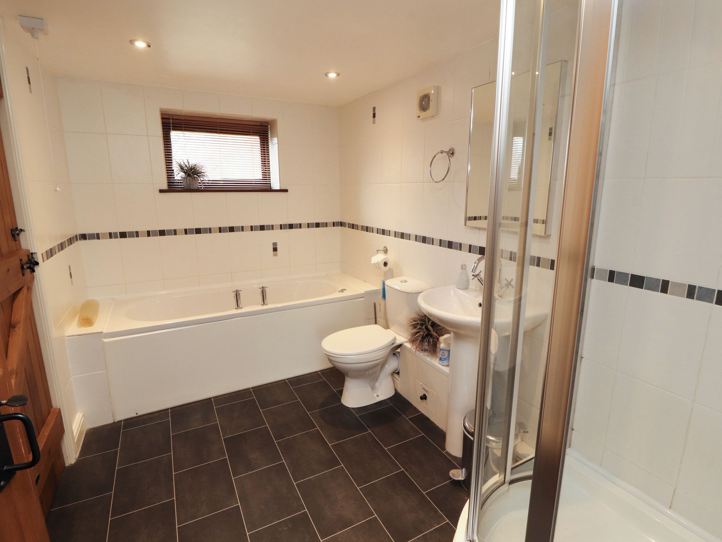 A bathroom with a bathtub, toilet, and sink, featuring dark floor tiles and a small window.