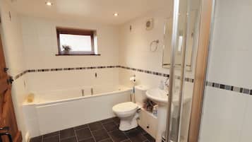 A bathroom with a bathtub, toilet, and sink, featuring dark floor tiles and a small window.