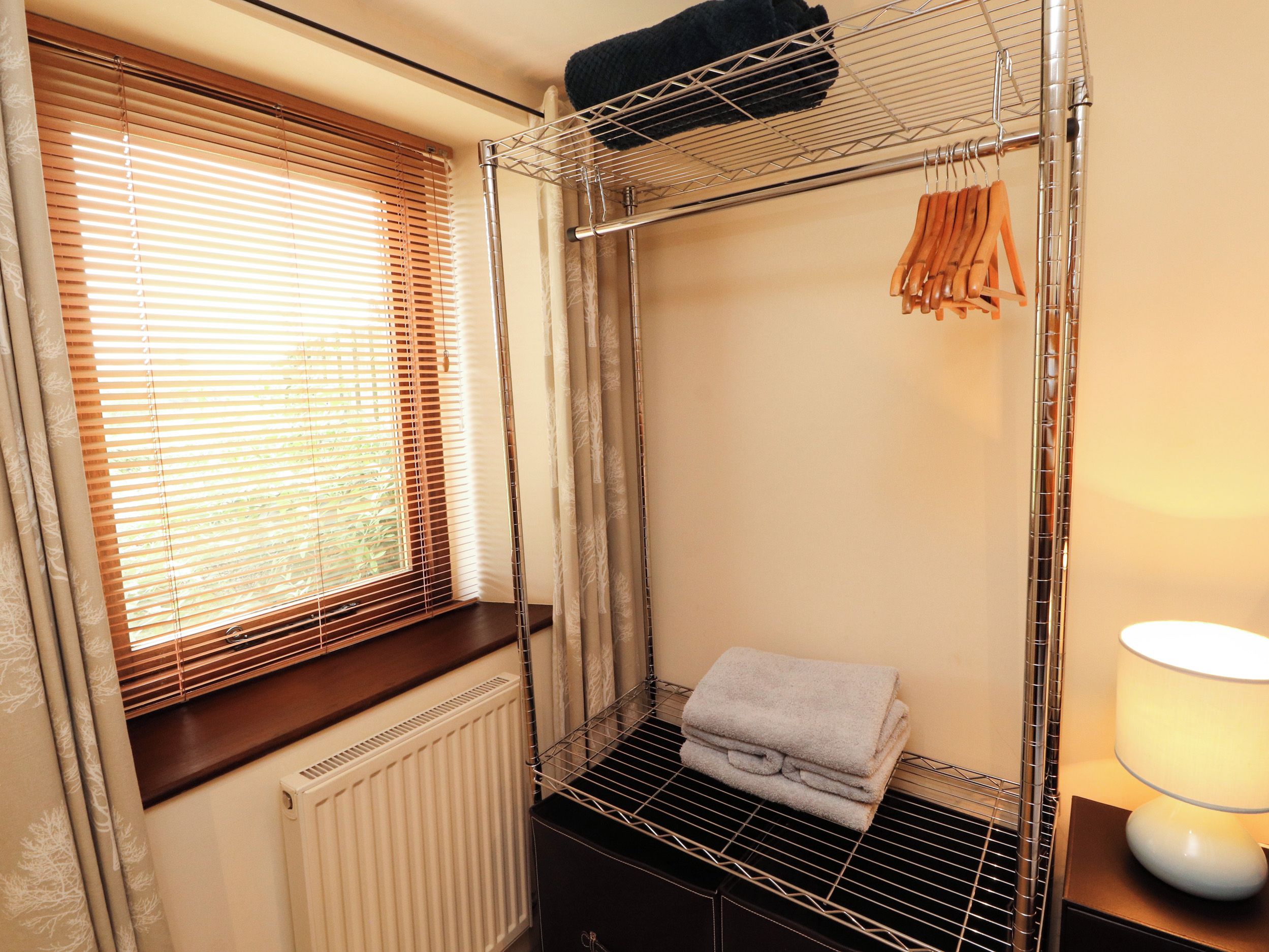 Et værelse med vindue, radiator, metalreol og lampe.