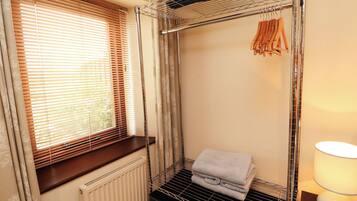 Et værelse med vindue, radiator, metalreol og lampe.