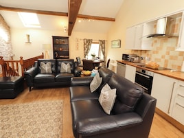 A living room with a black leather sofa, a dining area, and a kitchen with white cabinets and a wooden countertop.