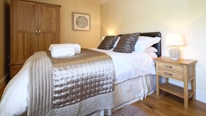 A bedroom with a bed, a nightstand, a wooden wardrobe, and a wall-mounted lamp. - Grove Cottage (Bishop Auckland)