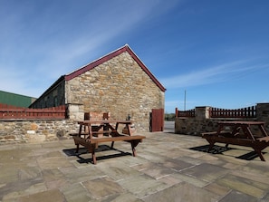 Enjoy outdoor dining at this rustic building with two picnic tables on a stone-paved surface.