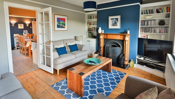 A living room with a fireplace, a sofa, a coffee table, and a bookshelf filled with books. - Wren Cottage (Harrogate)