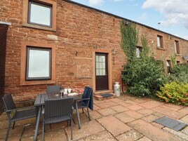 A stone building with a patio area featuring a table and chairs, a door, and a small garden with plants and flowers.