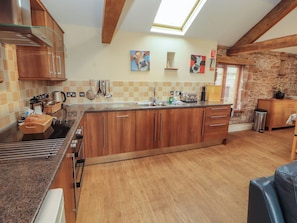 A kitchen with wooden cabinets, a central island, a skylight, and artwork on the walls. - Hayloft Cottage (Wigton)
