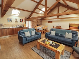 A spacious living area with a high ceiling, wooden beams, a dining table, and two blue leather sofas.
