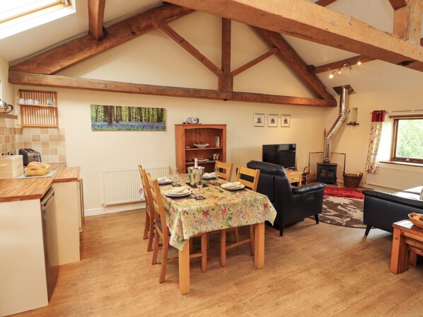 A dining area with a table set for four, wooden chairs, a black sofa, a television, and a fireplace. - Horseshoe Cottage (Wigton)