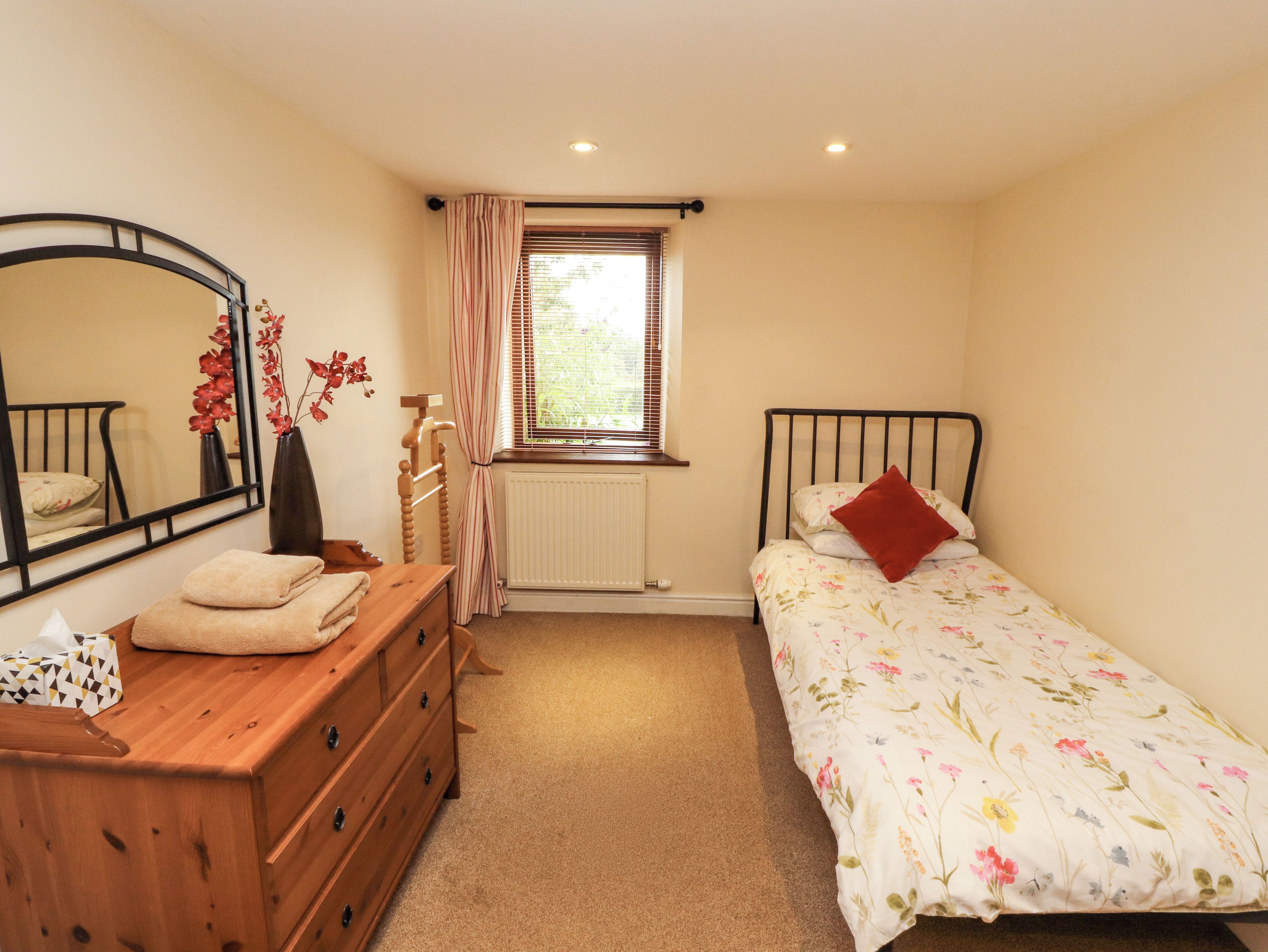 A bedroom with a bed, a dresser, a mirror, a radiator, and a window with curtains.