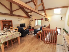A spacious living area with a wooden ceiling, a fireplace, a dining table set for four, and a staircase with a wooden railing.