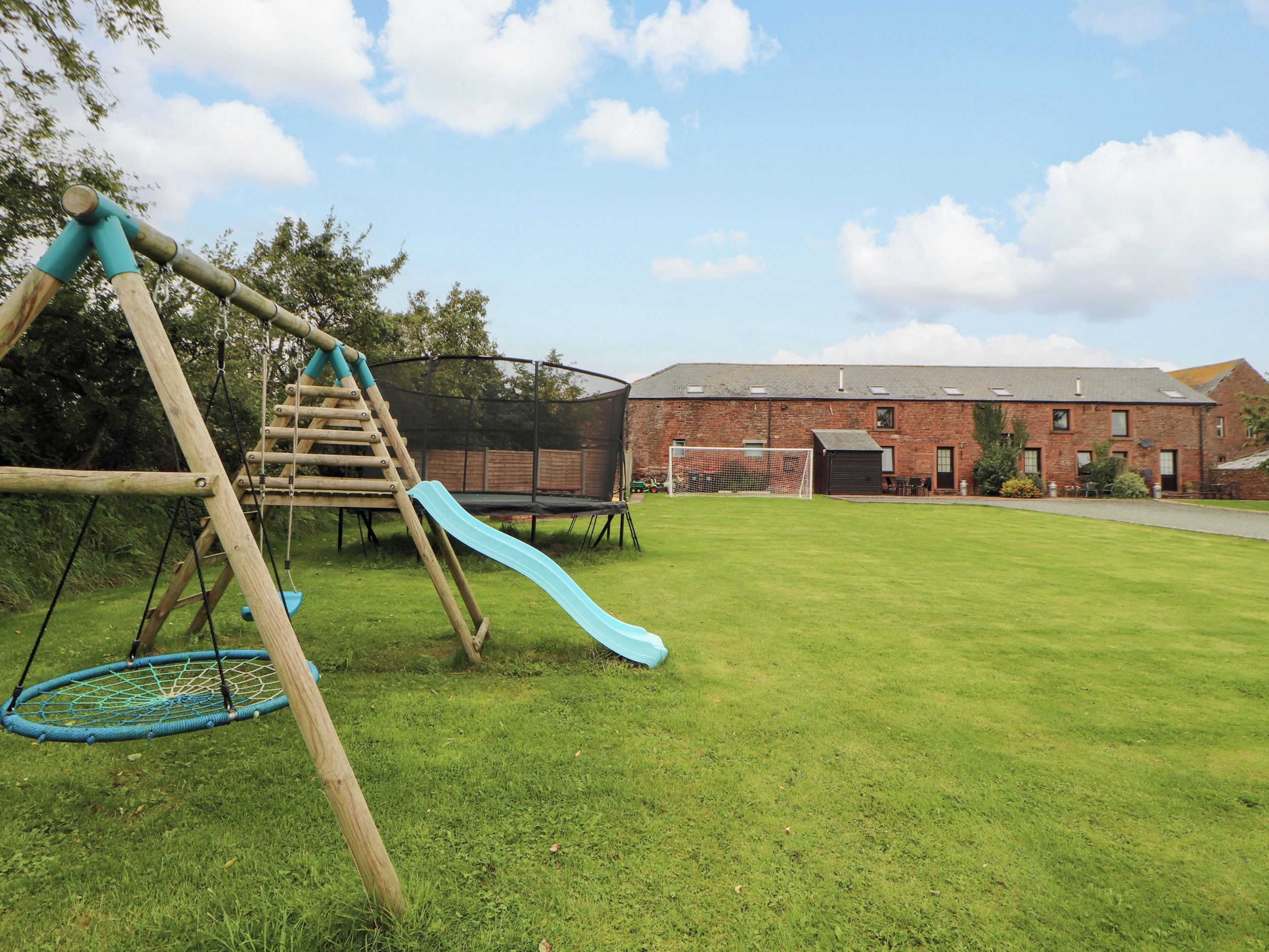 Un parque infantil con un tobogán y una estructura para escalar, un trampolín y un edificio al fondo.