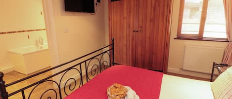 A bedroom with a bed, a wooden wardrobe, a television mounted on the wall, and a window with blinds.