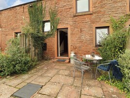 A stone building with a brick exterior, a wooden fence, and a small garden area with a metal table and chairs.