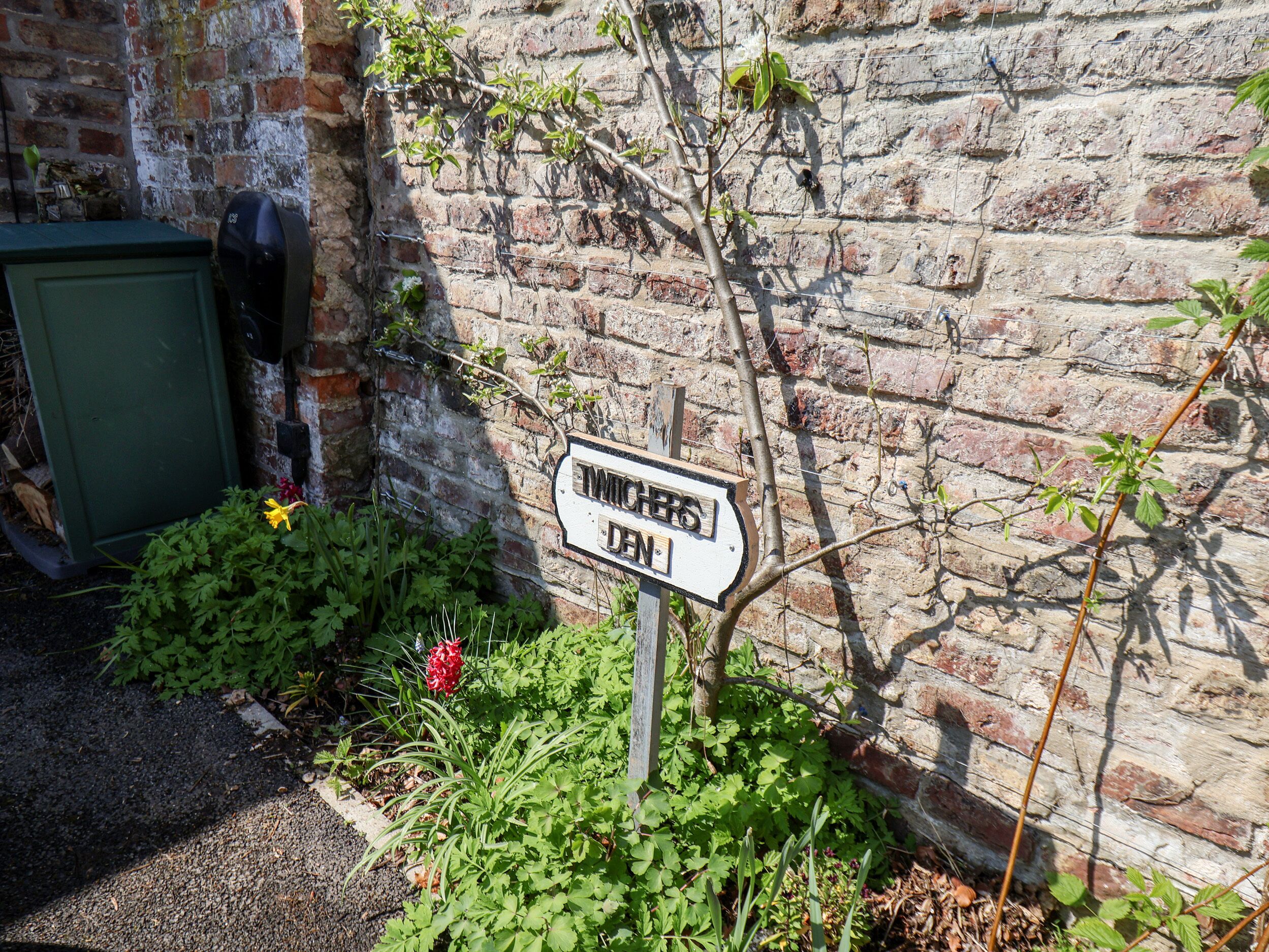 A signpost with the inscription "TWIGHERS DEN" against a brick wall.