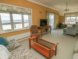 A living room with a sofa, a wooden coffee table, a television, and a view of the sea.