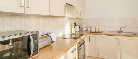 A modern kitchen with white cabinets, a wooden countertop, a built-in microwave, a toaster, and a sink.