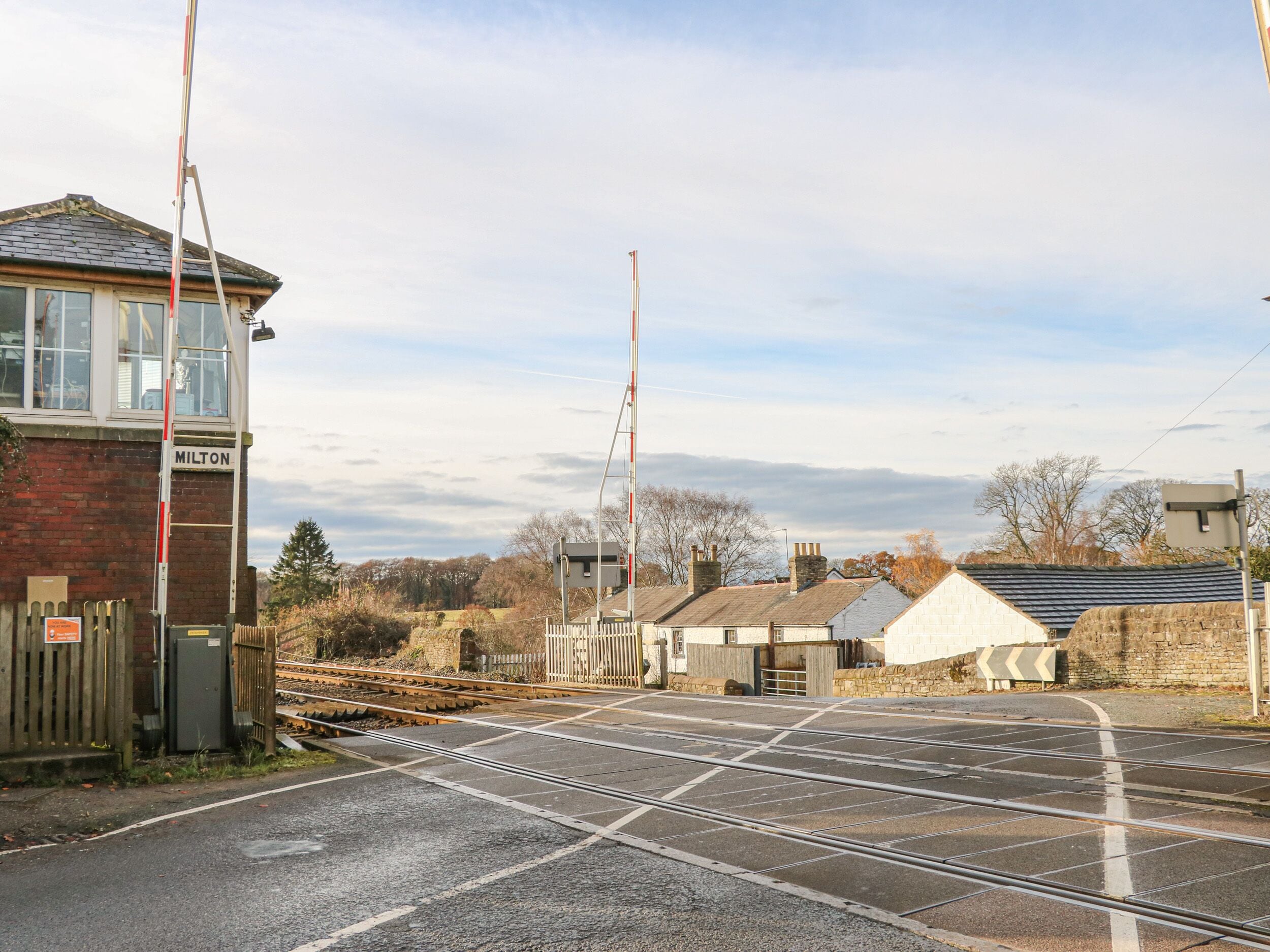 Un passage à niveau avec un poste de signalisation portant l’inscription « MILTON » et une clôture en bois.