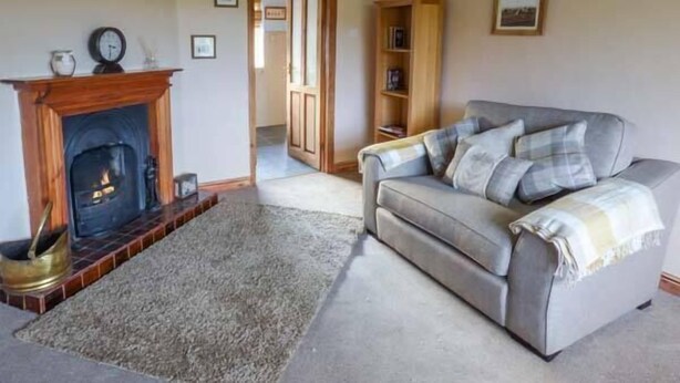 A living room with a fireplace, a grey sofa, and a wooden bookshelf. - Chapel Cottage (Whitby)