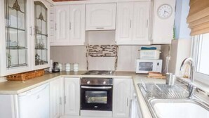 A compact kitchen with white cabinets, a microwave, a stove, and a sink. - Chapel Cottage (Whitby)