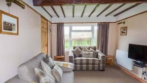 A living room with a sofa and armchair, a television, and a window with curtains. - Chapel Cottage (Whitby)