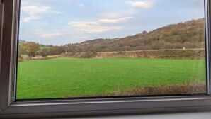 A view through a window of a green field with a hill in the background. - Chapel Cottage (Whitby)