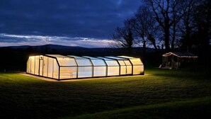 Una estructura tipo invernadero con techo transparente, rodeada de césped y árboles.