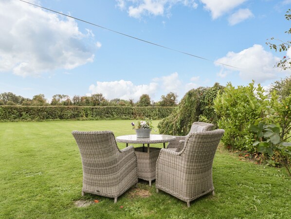 A patio with wicker furniture and a table, surrounded by a well-maintained lawn and hedges. - Pear Tree Cottage (Wedmore)