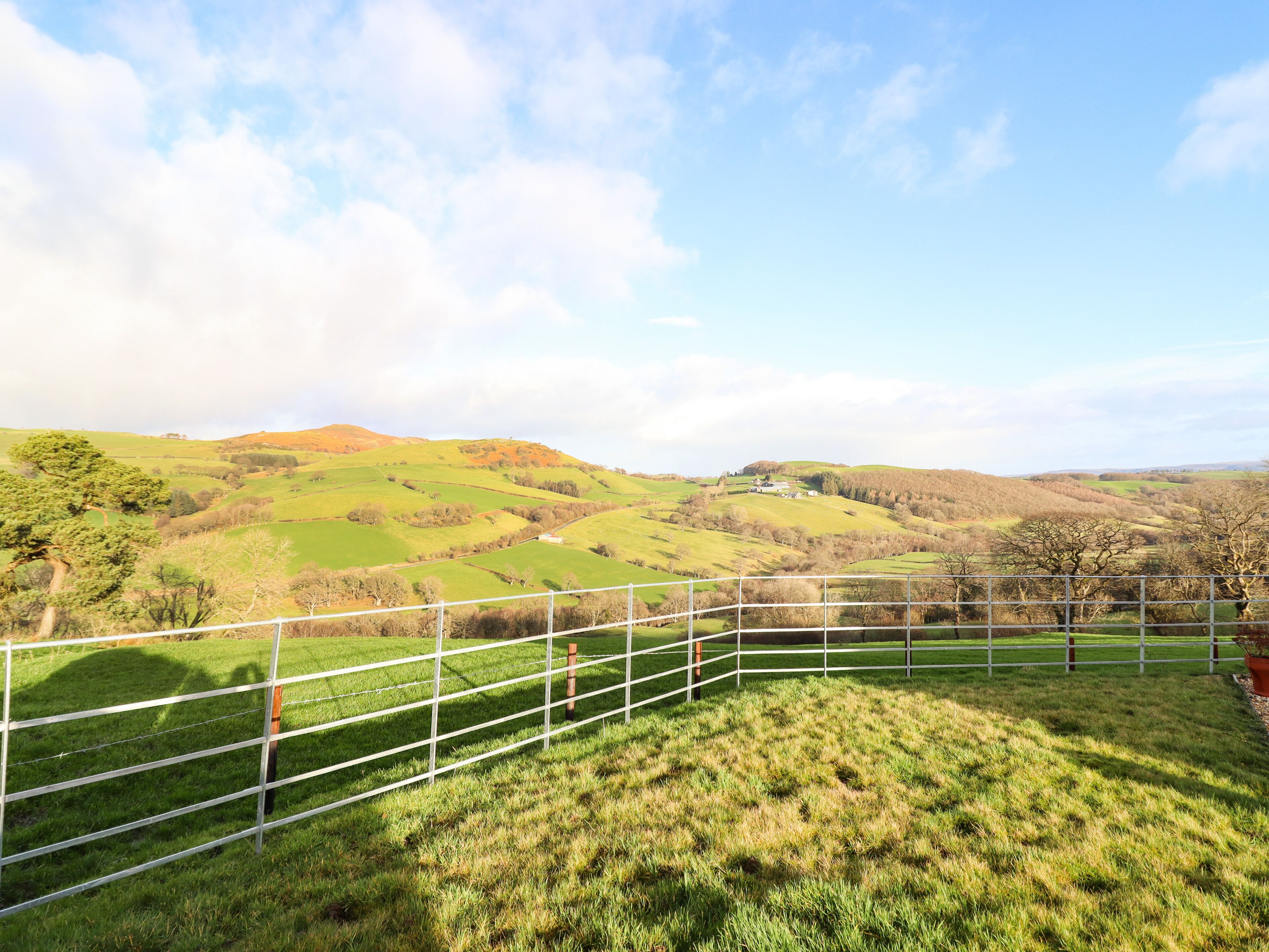 A fenced grassy area with a view of rolling hills and a distant building.
